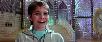 Movie still from “The NeverEnding Story II: The Next Chapter” (1990), directed by George Miller – A young man smiling in front of a staircase; Close Up shot, Low angle
