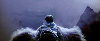 Movie still from “The NeverEnding Story II: The Next Chapter” (1990), directed by George Miller – A person sitting on a bench in front of a cloudy sky; Medium shot, High angle
