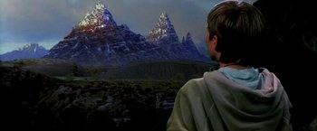 Movie still from “The NeverEnding Story II: The Next Chapter” (1990), directed by George Miller – A man standing in front of a mountain range; Medium shot, Over the shoulder angle