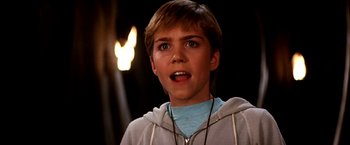 Movie still from “The NeverEnding Story II: The Next Chapter” (1990), directed by George Miller – A young man with short blonde hair wearing a blue shirt; Close Up shot, Low angle