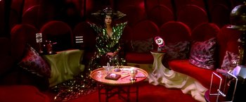 Movie still from “The NeverEnding Story II: The Next Chapter” (1990), directed by George Miller – A woman dressed as a witch sitting in front of a coffee table; Wide shot, High angle