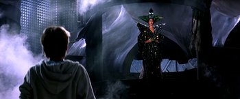Movie still from “The NeverEnding Story II: The Next Chapter” (1990), directed by George Miller – A woman dressed as the evil queen from snow white and the seven dwarfs; Medium shot, Over the shoulder angle
