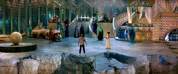 Movie still from “The NeverEnding Story II: The Next Chapter” (1990), directed by George Miller – A group of people standing around in a room; Extreme Wide shot, High angle