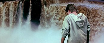 Movie still from “The NeverEnding Story II: The Next Chapter” (1990), directed by George Miller – A man standing in front of a large waterfall; Medium shot, Over the shoulder angle