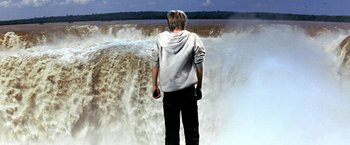 Movie still from “The NeverEnding Story II: The Next Chapter” (1990), directed by George Miller – A man standing in front of a large waterfall; Wide shot, Over the shoulder angle