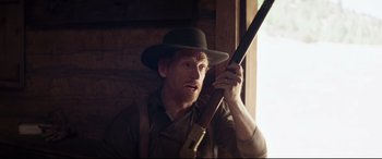 Movie still from “Hostiles” (2017), directed by Scott Cooper – A man holding a rifle in his hand and wearing a hat; Medium shot, Over the shoulder angle