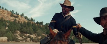 Movie still from “Hostiles” (2017), directed by Scott Cooper – A man riding on the back of a brown horse; Medium shot, Low angle