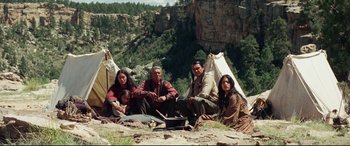 Movie still from “Hostiles” (2017), directed by Scott Cooper – A group of people sitting on the ground near some trees; Wide shot, High angle