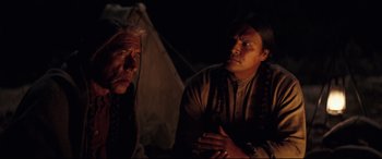 Movie still from “Hostiles” (2017), directed by Scott Cooper – Two native american men sitting in front of a tent at night; Medium shot, Over the shoulder angle