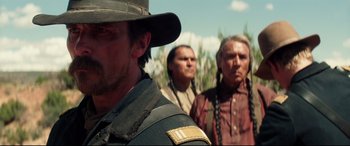 Movie still from “Hostiles” (2017), directed by Scott Cooper – A man in a cowboy hat standing in front of two men; Close Up shot, Over the shoulder angle