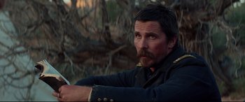 Movie still from “Hostiles” (2017), directed by Scott Cooper – A person sitting in a field; Close Up shot, Over the shoulder angle