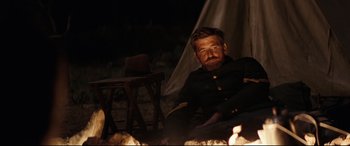 Movie still from “Hostiles” (2017), directed by Scott Cooper – A man sitting in front of a fire at night; Medium shot, Over the shoulder angle