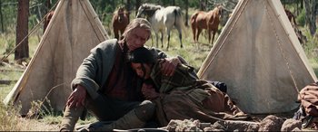 Movie still from “Hostiles” (2017), directed by Scott Cooper – A man and a woman sitting on the ground with horses in the background; Wide shot, High angle
