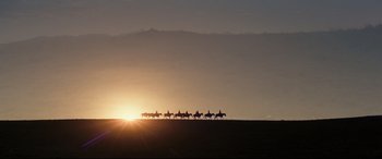 Movie still from “Hostiles” (2017), directed by Scott Cooper – A group of people on horseback riding across a field at sunset; Extreme Wide shot, Low angle