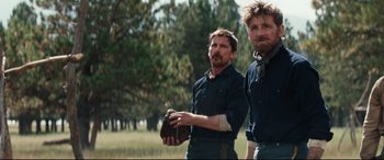 Movie still from “Hostiles” (2017), directed by Scott Cooper – A couple of men standing next to each other in a field; Medium shot, Over the shoulder angle