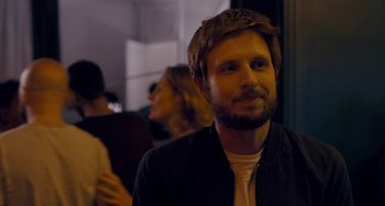 Movie still from “The Night Eats the World” (2018), directed by Dominique Rocher – A man with a goatee and a white shirt; Close Up shot, Over the shoulder angle