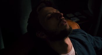 Movie still from “The Night Eats the World” (2018), directed by Dominique Rocher – A man with a beard is laying down in the dark; Close Up shot, High angle