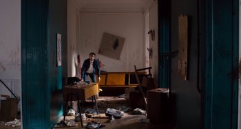 Movie still from “The Night Eats the World” (2018), directed by Dominique Rocher – A man is in a room that has a lot of debris on the floor; Wide shot, High angle