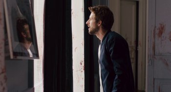 Movie still from “The Night Eats the World” (2018), directed by Dominique Rocher – A man standing in front of a window looking up; Medium shot, Over the shoulder angle