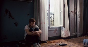 Movie still from “The Night Eats the World” (2018), directed by Dominique Rocher – A man sitting on the floor in front of a window; Medium shot, High angle