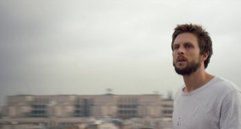 Movie still from “The Night Eats the World” (2018), directed by Dominique Rocher – A man standing on top of a building looking into the distance; Close Up shot, Low angle