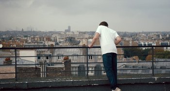Movie still from “The Night Eats the World” (2018), directed by Dominique Rocher – A man standing on a balcony looking over a city; Wide shot, Low angle