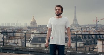 Movie still from “The Night Eats the World” (2018), directed by Dominique Rocher – A man standing on a roof top in front of the eiffel tower; Medium shot, Low angle