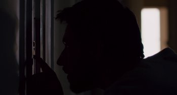 Movie still from “The Night Eats the World” (2018), directed by Dominique Rocher – A man with a goatee looking out of a window; Extreme Close Up shot, Over the shoulder angle
