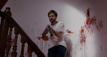 Movie still from “The Night Eats the World” (2018), directed by Dominique Rocher – A man holding a video game controller in front of a wall covered in blood; Medium shot, Low angle