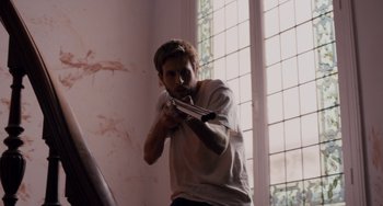 Movie still from “The Night Eats the World” (2018), directed by Dominique Rocher – A man holding a knife in his mouth; Medium shot, Low angle
