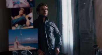 Movie still from “The Night Eats the World” (2018), directed by Dominique Rocher – A man wearing a leather jacket standing in front of a window; Medium shot, Over the shoulder angle