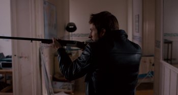 Movie still from “The Night Eats the World” (2018), directed by Dominique Rocher – A man in a leather jacket holding a gun; Medium shot, Over the shoulder angle