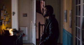 Movie still from “The Night Eats the World” (2018), directed by Dominique Rocher – A man standing in front of an open door; Medium shot, Over the shoulder angle