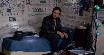 Movie still from “The Night Eats the World” (2018), directed by Dominique Rocher – A man sitting on top of a bed in a room; Medium shot, High angle
