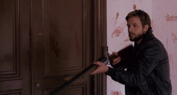 Movie still from “The Night Eats the World” (2018), directed by Dominique Rocher – A man holding a gun in front of a door; Medium shot, Over the shoulder angle