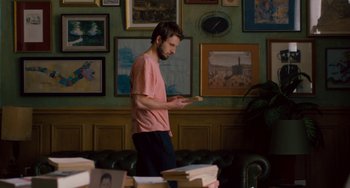 Movie still from “The Night Eats the World” (2018), directed by Dominique Rocher – A man standing in front of a bunch of books; Wide shot, Over the shoulder angle
