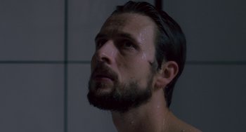 Movie still from “The Night Eats the World” (2018), directed by Dominique Rocher – A person with a beard in the shower; Close Up shot, Low angle