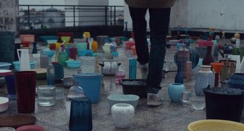 Movie still from “The Night Eats the World” (2018), directed by Dominique Rocher – A person walking on the ground with many vases on the ground; Wide shot, High angle