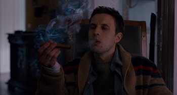 Movie still from “The Night Eats the World” (2018), directed by Dominique Rocher – A man smoking a cigar while sitting on a couch; Medium shot, Low angle