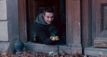 Movie still from “The Night Eats the World” (2018), directed by Dominique Rocher – A young man holding a box in front of an open window; Medium shot, Low angle