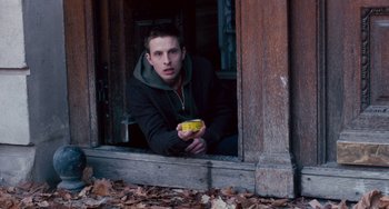 Movie still from “The Night Eats the World” (2018), directed by Dominique Rocher – A young man holding a banana looking out of a window; Medium shot, Low angle