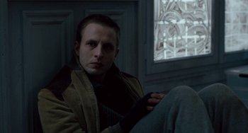 Movie still from “The Night Eats the World” (2018), directed by Dominique Rocher – A man sitting on the floor in front of a window; Close Up shot, High angle