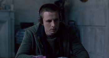 Movie still from “The Night Eats the World” (2018), directed by Dominique Rocher – A man with headphones sitting at a table; Close Up shot, Over the shoulder angle