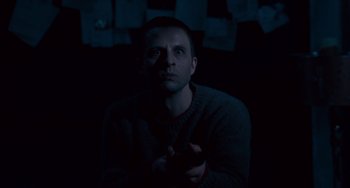 Movie still from “The Night Eats the World” (2018), directed by Dominique Rocher – A man in a dark room holding a cell phone; Medium shot, High angle