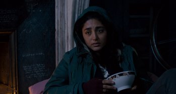 Movie still from “The Night Eats the World” (2018), directed by Dominique Rocher – A woman in a green jacket holding a white bowl; Medium shot, Over the shoulder angle