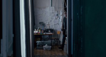 Movie still from “The Night Eats the World” (2018), directed by Dominique Rocher – A man standing next to a table with papers on it; Wide shot, Over the shoulder angle