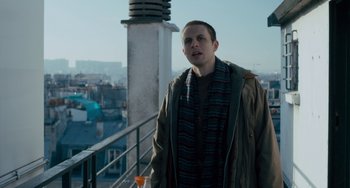 Movie still from “The Night Eats the World” (2018), directed by Dominique Rocher – A man standing on top of a building next to a balcony; Medium shot, Low angle