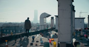 Movie still from “The Night Eats the World” (2018), directed by Dominique Rocher – A man standing on a rooftop looking out at a city; Extreme Wide shot, Low angle