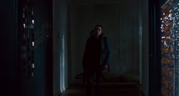 Movie still from “The Night Eats the World” (2018), directed by Dominique Rocher – A woman standing in a dark room in front of a door; Wide shot, Low angle