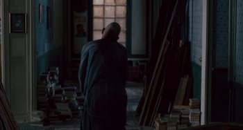 Movie still from “The Night Eats the World” (2018), directed by Dominique Rocher – A man standing in front of stacks of books in a room; Wide shot, High angle